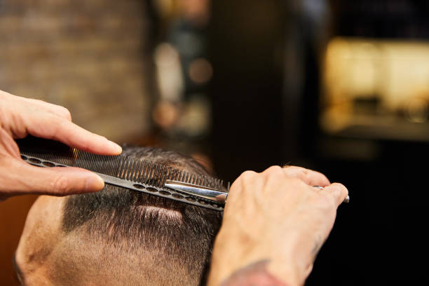 Side view of an unrecognizable barber cutting the hair of a male client with professional scissors in a beauty salon.