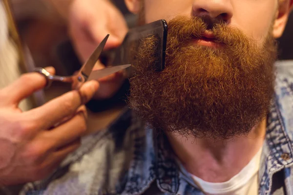 close up photo of barber cutting clients beard with scissor