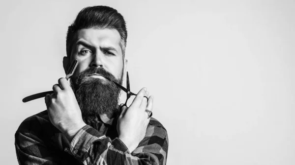 bearded man holding razor and scissor