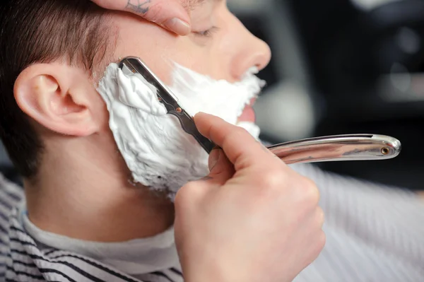barber shaving a mans beard with a shave cream