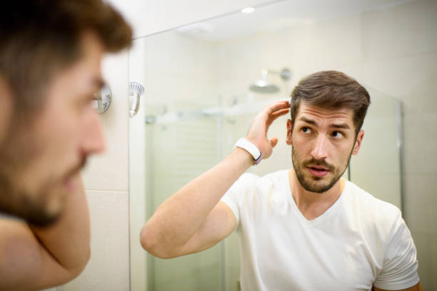 Young man in the bathroom looking in the mirror and fixing his hair.