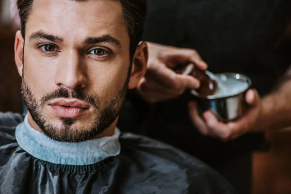 man staring while barber preparing shaving cream