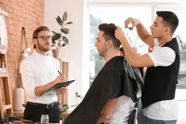 student cutting clients hair while master barber watching and grading