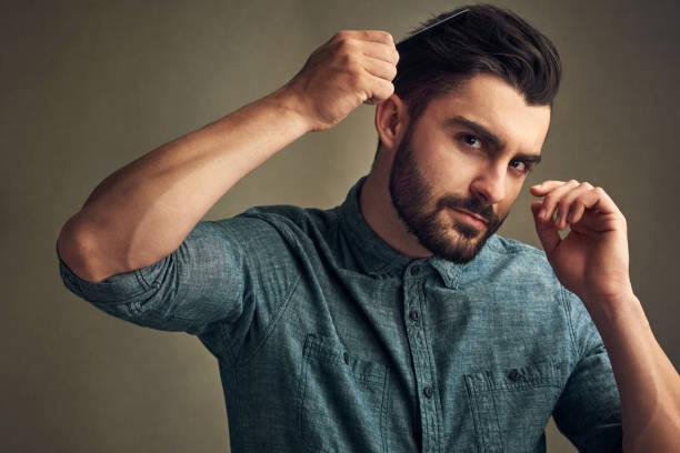 Studio shot of a handsome young man combing his hair against a grey background